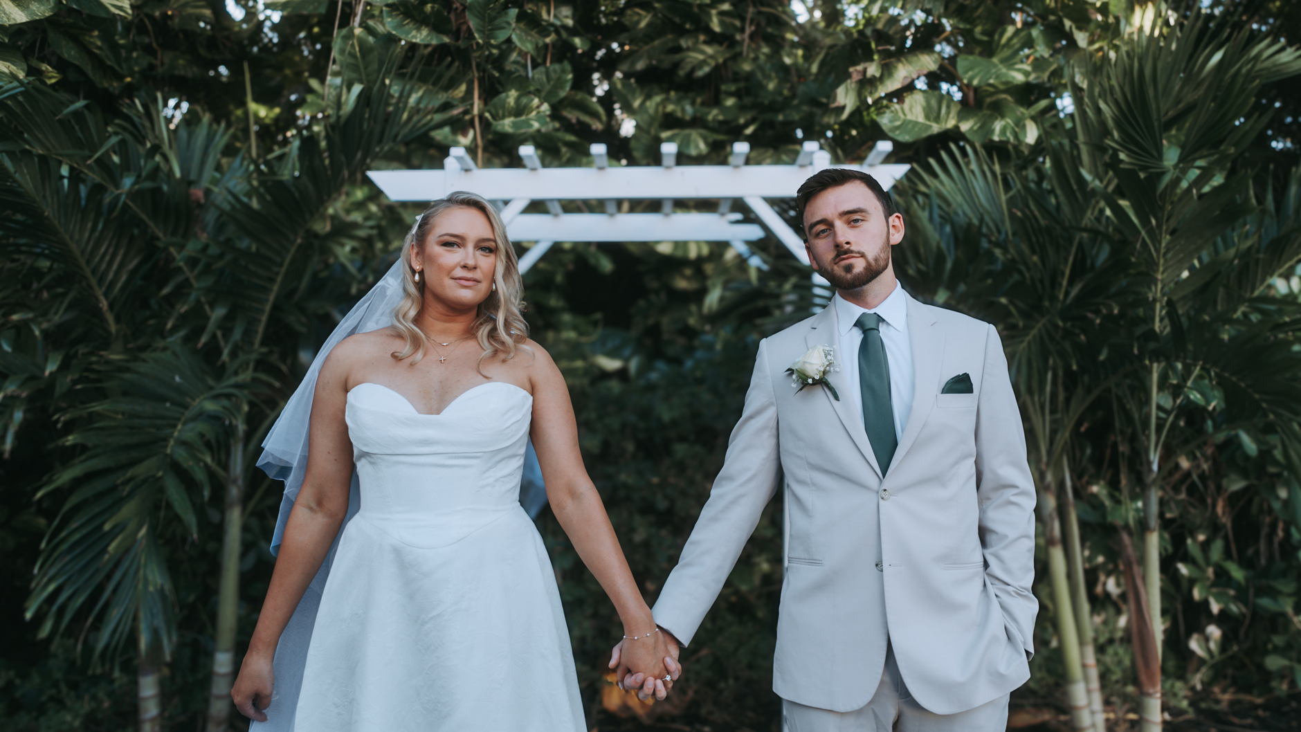 A bride and groom holding hands under a white arch in an outdoor wedding setting.