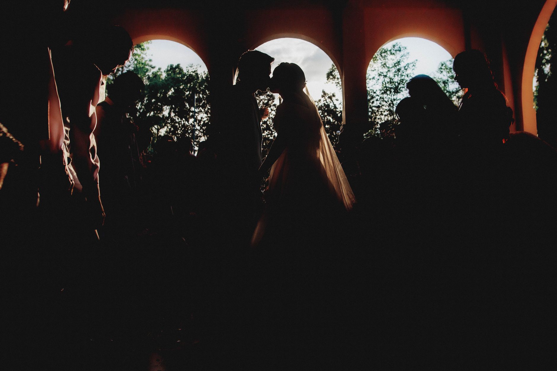 Silhouette of newlyweds kissing in a dramatic wedding ceremony setting.